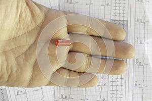 Hands of a man holding a red capsule on an electrocardiogram. Drugs of legal use for humans