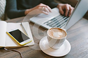 Hands of man on laptop with coffee and smartphone with notepad