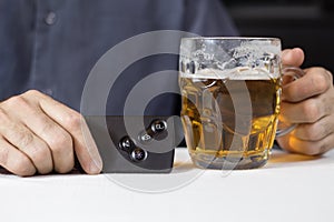Hands of the man in one hand hold the key card in the car, in the second mug with beer.