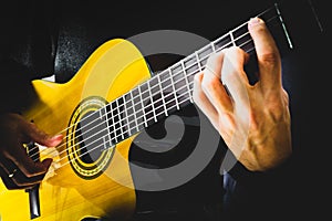 Hands of a man playing acoustic guitar on a black background