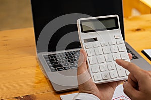 Hands of a man pressing a calculator and making money at the home office by writing a report on his laptop. business man`s hand ca