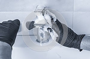 Hands of man in protective gloves cleaning tap at bathroom.