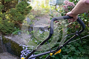 Hands of man pushing lawnmower through small backyard in spring