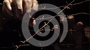 Hands of a man shaking rusty barbed wire in the dark lit by hard light. 4K video.