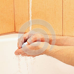 Hands of man with soap under running water in bathroom