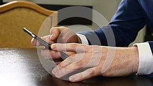 Hands of man in suit holding black smartphone. Male fingers tapping mobile phone screen. Contactless payment. man is