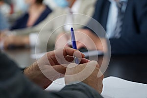 Hands of a man in a suit holding a fountain pen during a business meeting. An official, deputy, lawyer or businessman. Reportage.