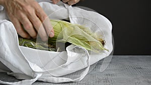 Hands of man take and put out ear of corn from fabric tote bag on tabletop