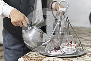 Hands of man tea maker with metal Turkish teapot pouring tea into glass cups in a coffee house in Turkey