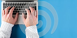 Hands of man typing on laptop computer on blue desk background