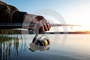 Hands of a man in a Urp plan hold a fishing rod, a fisherman catches fish at dawn. Fishing hobby vacation concept. Copy space
