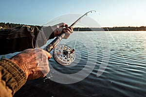 Hands of a man in a Urp plan hold a fishing rod, a fisherman catches fish at dawn. Fishing hobby vacation concept. Copy space