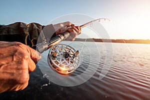 Hands of a man in a Urp plan hold a fishing rod, a fisherman catches fish at dawn. Fishing hobby vacation concept. Copy space