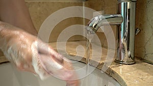 Hands of man wash their hands in a sink with foam to wash the skin and water flows through the hands. Concept of health