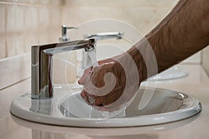 Hands of a man washing his hands under running water from a faucet