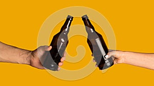 Hands of man and woman clinking bottles of beer, celebrating something on orange background, mockup for design