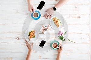 Hands of man and woman drinking coffee with croissants