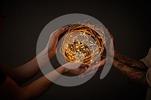 Hands of a man and a woman holding a wreath of branches with yellow Christmas lights around a black background