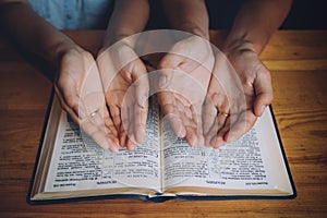 Hands of man and woman praying over the open bible