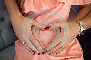 Hands of man and woman on pregnant belly in the shape of heart
