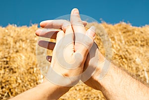 The hands of a man and a woman are woven together against a background of straw and a blue sky in the summer