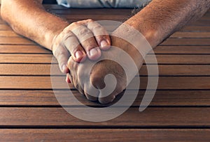 Hands of a man on a wooden table. Clenched fist showing pain