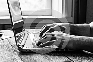 Hands of a man working at a computer laptop at the window