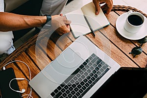 Hands of a man working at a laptop top view of a workspace, on a wooden table with a smartphone a cup of coffee and a notebook for