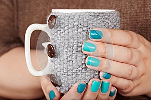 Hands with manicured nails holding a tea cup with knitted cover