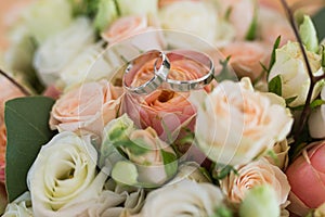 Hands of married couple with golden rings.Two wedding golden rings lying on a wedding bouquets with orange and beige roses