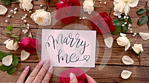 Hands with MARRY ME card between roses