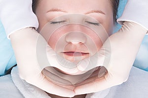 Hands of a massage therapist working on the neck and face area, top view