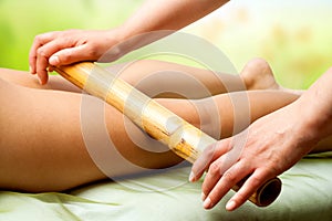 Hands massaging female legs with bamboo.