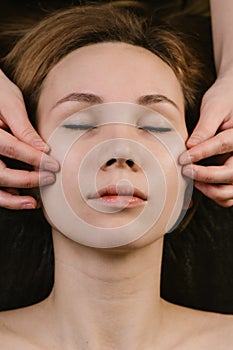 Hands massaging woman`s cheeks with fingers at asian beauty clinic. Top view photo