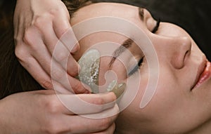 Young woman having a gua sha face massage at asian beauty clinic. Side view photo