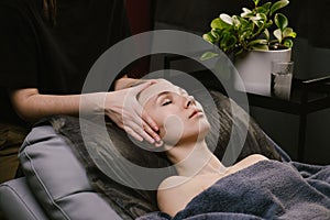 Hands massaging young woman`s head while she`s lying on a leather pillow