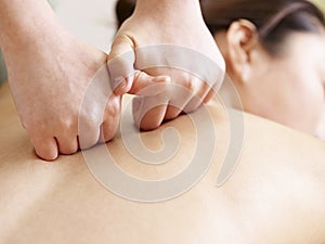 Hands of masseur performing massage on young asian woman