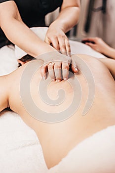 Hands of a masseuse on a female back during work - spa treatments for female beauty and health