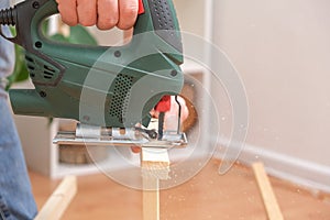 The hands of a master carpenter with an electric jigsaw in his hands cutting off a piece of wood. Male hands using fret