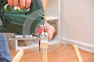 The hands of a master carpenter with an electric jigsaw in his hands cutting off a piece of wood. Male hands using fret