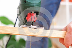 The hands of a master carpenter with an electric jigsaw in his hands cutting off a piece of wood. Male hands using fret