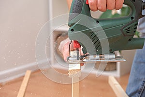 The hands of a master carpenter with an electric jigsaw in his hands cutting off a piece of wood. Male hands using fret