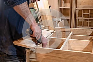 hands of a master carpenter install the hinges on the cabinet with a hand-held power tool screwdriver. Production of handmade photo