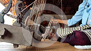 Hands of mature Asian woman spinning cotton with old traditional wheels machine in Thailand
