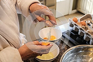 Hands of mature woman in bathrobe separating eggs on island in kitchen - Selective focus