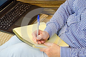 Hands of mature woman writing information from laptop into notepad. online learning, freelancing