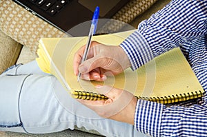 Hands of mature woman writing information from laptop into notepad. online learning, freelancing