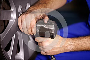Hands, mechanic and change wheel in shop, electric drill and car service or auto repairs for maintenance. Technician