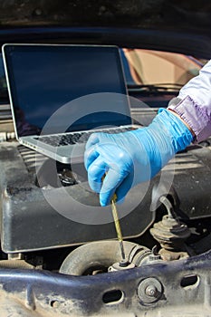 Hands of a mechanic with gloves doing a check up of a car`s diesel engine with tools and wrenches and laptop