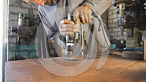 Hands of mechanic hold tool during operation. Man works in his garage or workshop. Worker processes detail on desktop